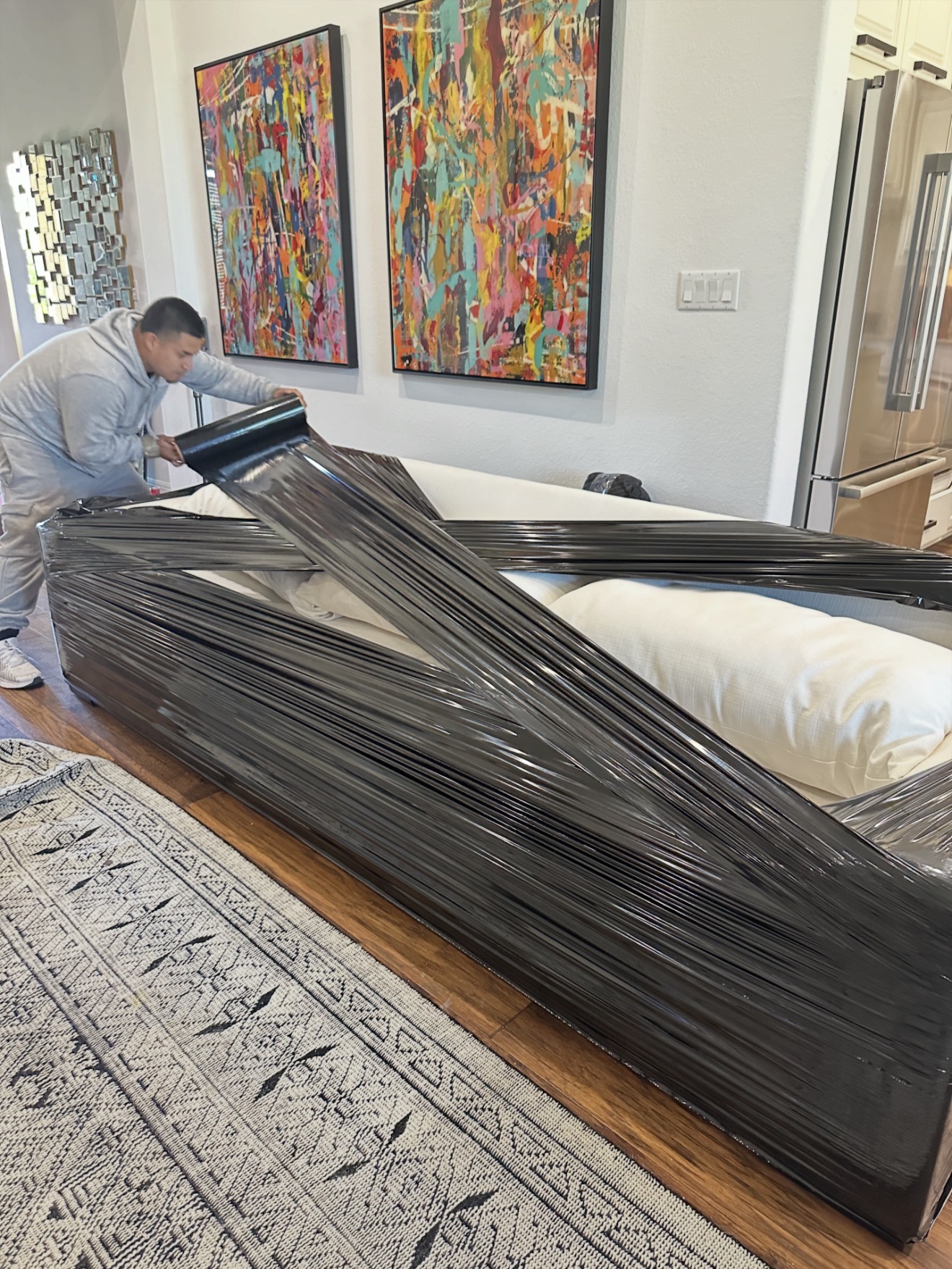 Gio, the owner of Gio's Moving, stretch-wrapping a white sofa before a move in Kyle, TX