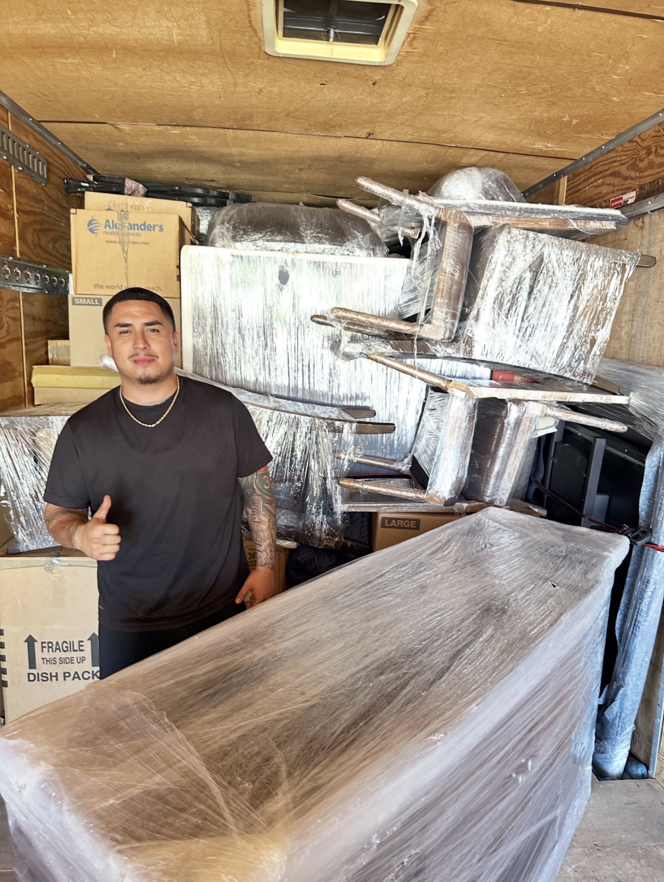 Gio giving a thumbs-up beside carefully wrapped furniture inside the moving truck