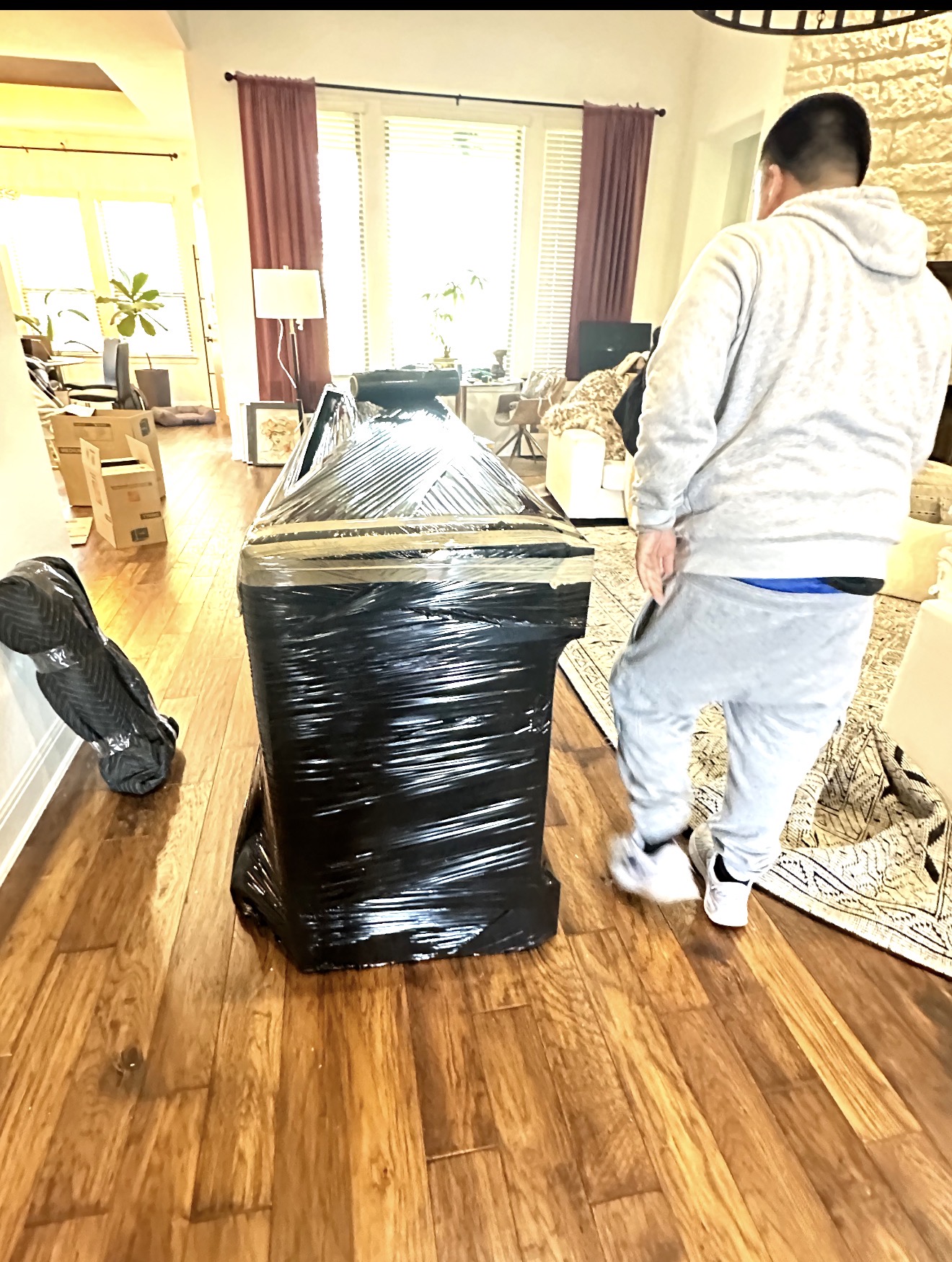 Gio moving a large wrapped furniture piece across hardwood floors during a local move